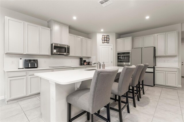 kitchen with sink, an island with sink, light tile patterned floors, a breakfast bar area, and stainless steel appliances