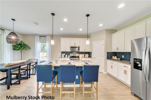 kitchen with appliances with stainless steel finishes, pendant lighting, backsplash, and white cabinets