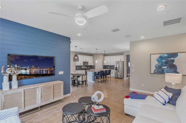 living room featuring wooden walls, ceiling fan, and light wood-type flooring