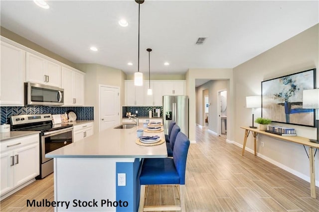 kitchen with light hardwood / wood-style flooring, white cabinetry, hanging light fixtures, a kitchen island with sink, and stainless steel appliances