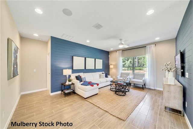 living room featuring light hardwood / wood-style floors, ceiling fan, and wood walls