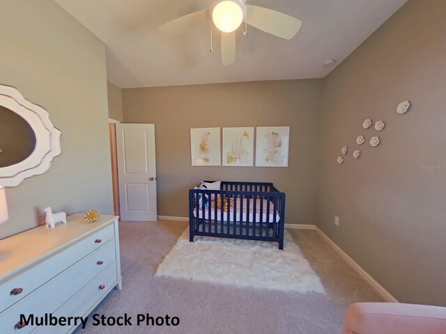 bedroom featuring ceiling fan, a nursery area, and light carpet