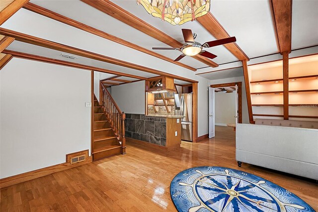 unfurnished living room with ceiling fan, built in shelves, beamed ceiling, and hardwood / wood-style floors