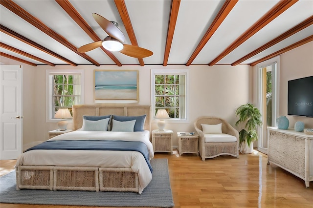 bedroom featuring multiple windows, beamed ceiling, and light wood-type flooring