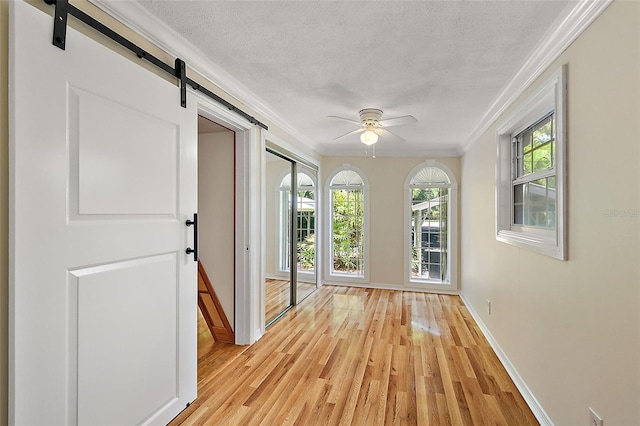 hallway with light wood-type flooring, a wealth of natural light, a barn door, and ornamental molding