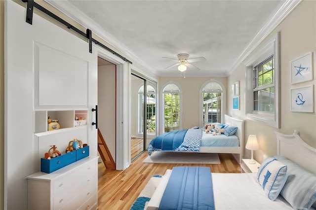 bedroom featuring light hardwood / wood-style flooring, ceiling fan, ornamental molding, and a barn door