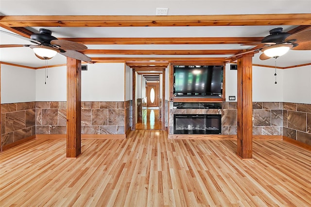 unfurnished living room featuring ceiling fan, light hardwood / wood-style flooring, beam ceiling, a tiled fireplace, and crown molding