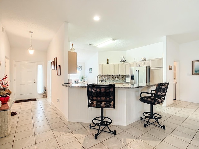 kitchen featuring decorative light fixtures, lofted ceiling, dark stone counters, a kitchen bar, and stainless steel fridge with ice dispenser