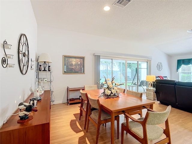 dining space with vaulted ceiling, a textured ceiling, a healthy amount of sunlight, and light hardwood / wood-style floors