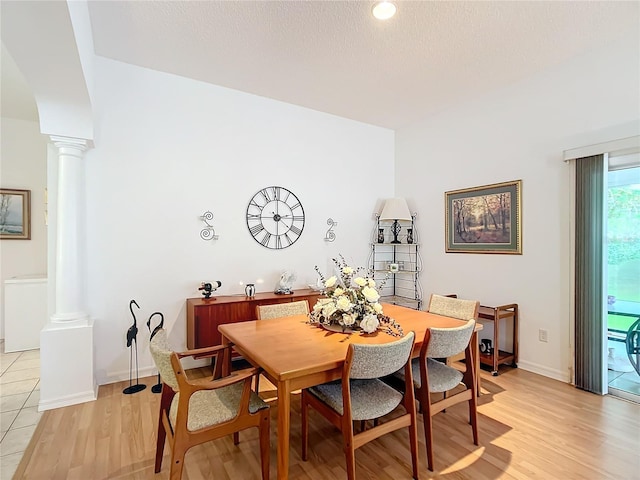 dining room featuring a textured ceiling, light hardwood / wood-style flooring, and ornate columns