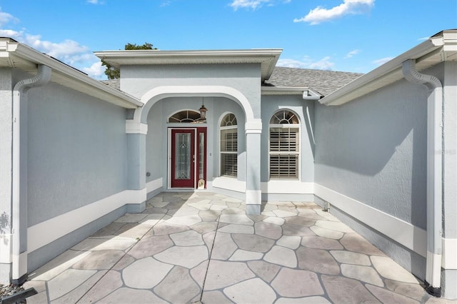 property entrance featuring roof with shingles and stucco siding