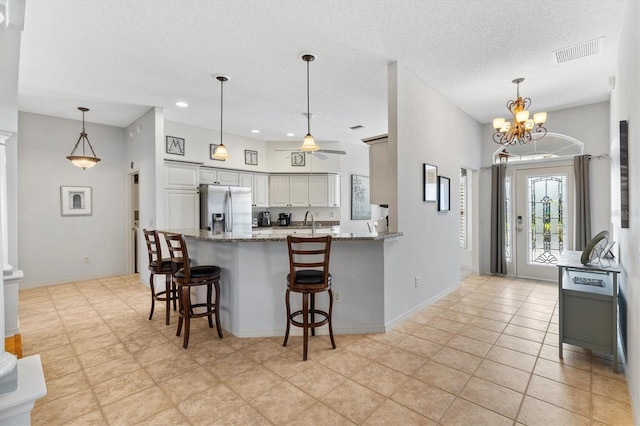 kitchen with light tile patterned flooring, ceiling fan with notable chandelier, stainless steel fridge, and kitchen peninsula