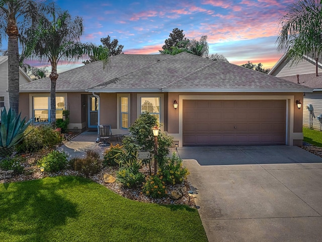 ranch-style home featuring a garage, concrete driveway, a yard, roof with shingles, and stucco siding