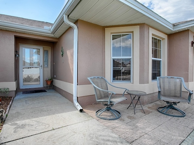 property entrance featuring a patio, roof with shingles, and stucco siding