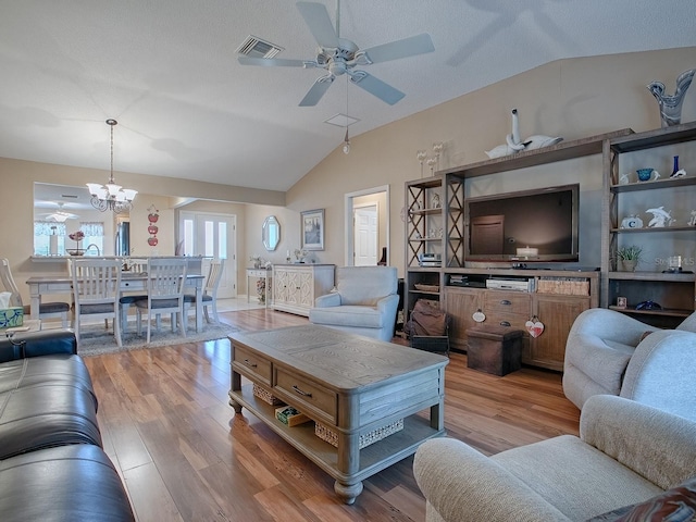 living room featuring ceiling fan with notable chandelier, lofted ceiling, visible vents, and wood finished floors