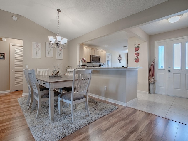 dining room with a textured ceiling, a notable chandelier, light hardwood / wood-style floors, and vaulted ceiling