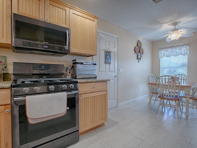 kitchen with stainless steel appliances, light stone counters, a textured ceiling, light brown cabinetry, and ceiling fan