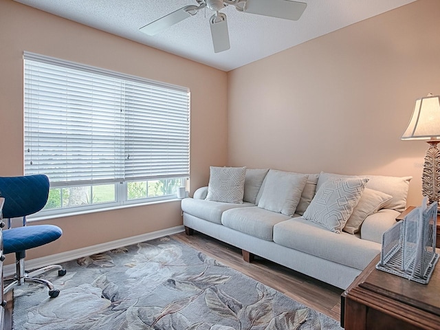 living room with a textured ceiling, ceiling fan, wood finished floors, and baseboards