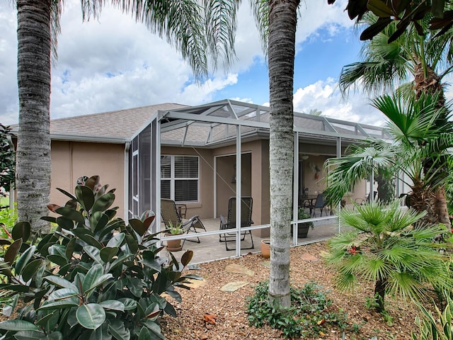 view of front of house featuring glass enclosure, a shingled roof, a patio area, and stucco siding