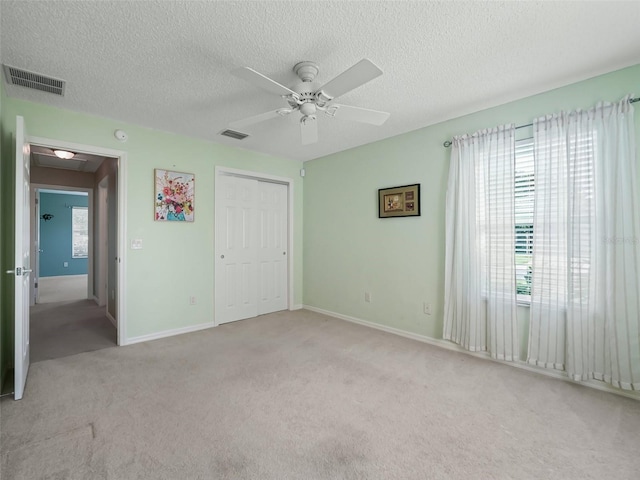 unfurnished bedroom with light carpet, a textured ceiling, ceiling fan, and a closet