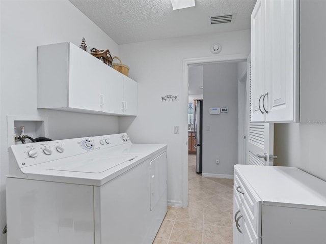 laundry room featuring washer and dryer, cabinets, light tile patterned floors, and a textured ceiling