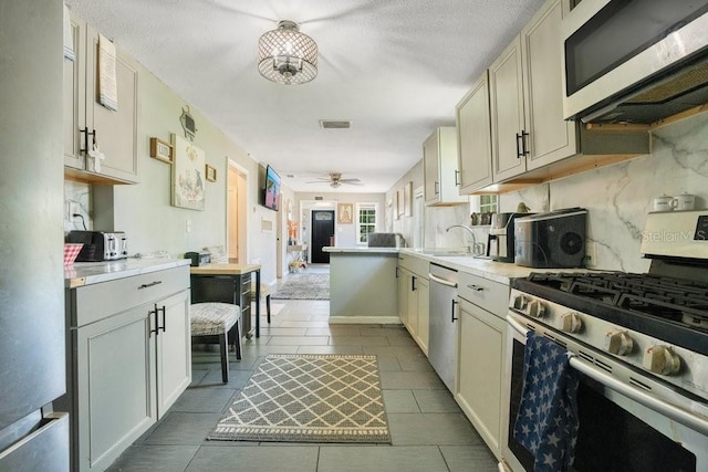 kitchen with appliances with stainless steel finishes, sink, backsplash, ceiling fan, and kitchen peninsula