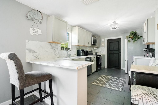 kitchen with kitchen peninsula, sink, appliances with stainless steel finishes, a kitchen breakfast bar, and decorative backsplash