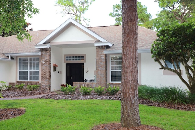 view of front of home featuring brick siding, a front lawn, and a shingled roof