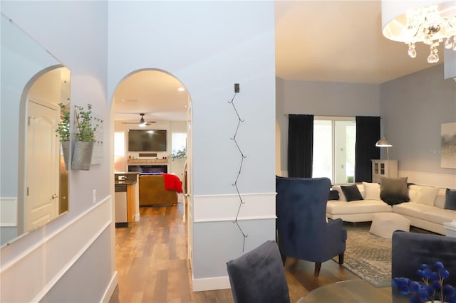 living area with arched walkways, ceiling fan with notable chandelier, and wood finished floors