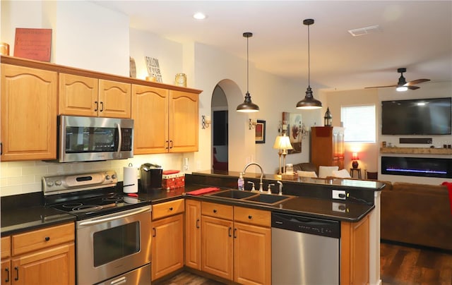 kitchen featuring stainless steel appliances, dark countertops, open floor plan, a sink, and a peninsula