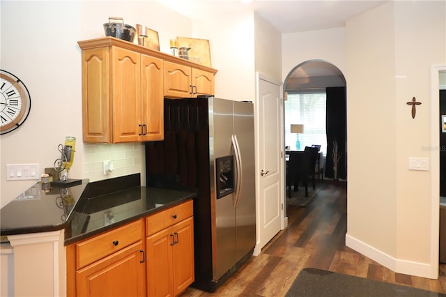 kitchen with dark stone counters, backsplash, dark wood-type flooring, stainless steel refrigerator with ice dispenser, and kitchen peninsula