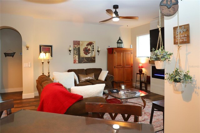 living room featuring a ceiling fan, arched walkways, baseboards, and wood finished floors