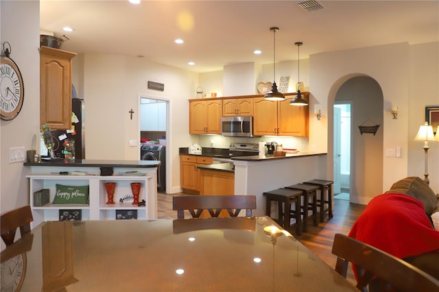 kitchen with dark wood-type flooring, a kitchen bar, appliances with stainless steel finishes, decorative light fixtures, and washer / clothes dryer