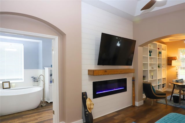 living area with ceiling fan, a glass covered fireplace, and wood finished floors