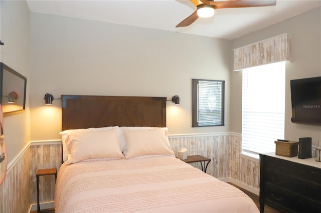 bedroom with ceiling fan, wooden walls, wood finished floors, and wainscoting