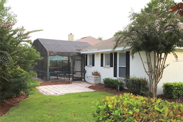 rear view of property with glass enclosure, a patio, a yard, stucco siding, and a chimney