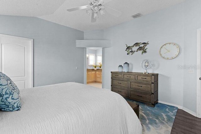 bedroom with ceiling fan, ensuite bath, hardwood / wood-style flooring, a textured ceiling, and lofted ceiling