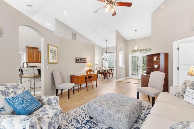 living room featuring high vaulted ceiling, ceiling fan with notable chandelier, and light wood-type flooring