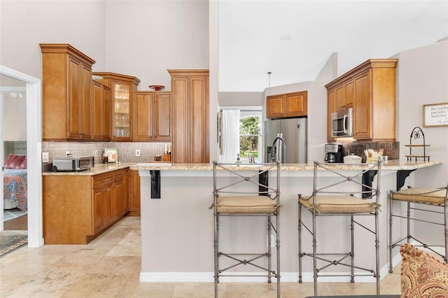 kitchen featuring light stone countertops, appliances with stainless steel finishes, a kitchen bar, kitchen peninsula, and a high ceiling