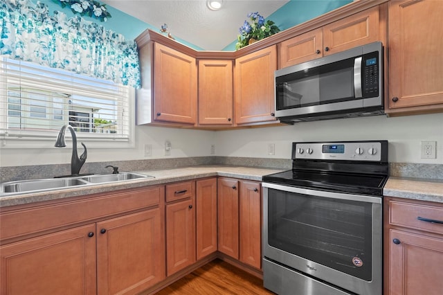 kitchen with stainless steel appliances, a sink, light wood-style floors, light countertops, and brown cabinetry