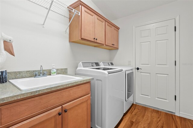 clothes washing area with sink, light hardwood / wood-style flooring, independent washer and dryer, and cabinets