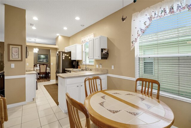 32915 Crooked Oaks Ln, Leesburg, FL 34748 - kitchen with light tile patterned floors, white cabinets, freestanding refrigerator, light countertops, and a sink