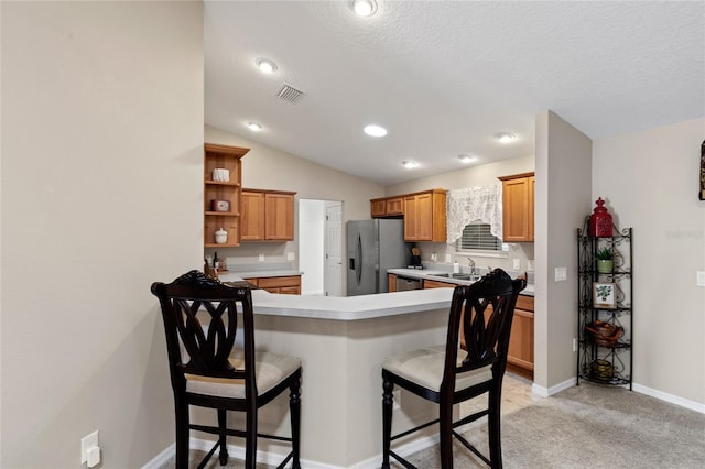 kitchen with visible vents, a breakfast bar area, a peninsula, light countertops, and stainless steel refrigerator with ice dispenser