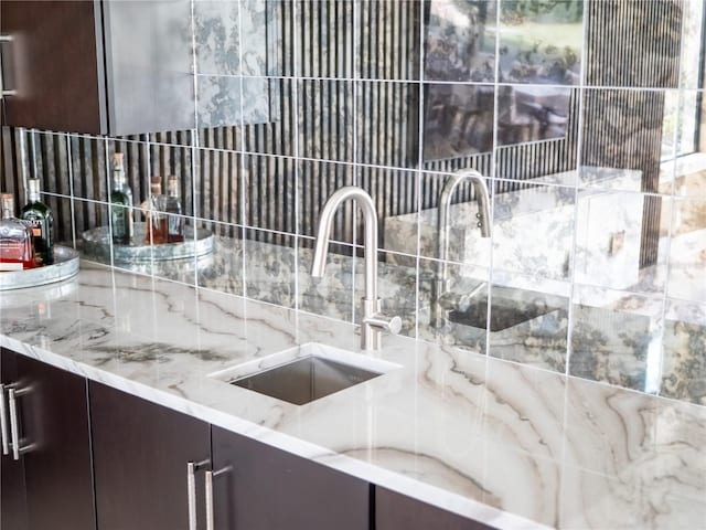 kitchen with decorative backsplash, dark brown cabinets, light stone counters, and sink