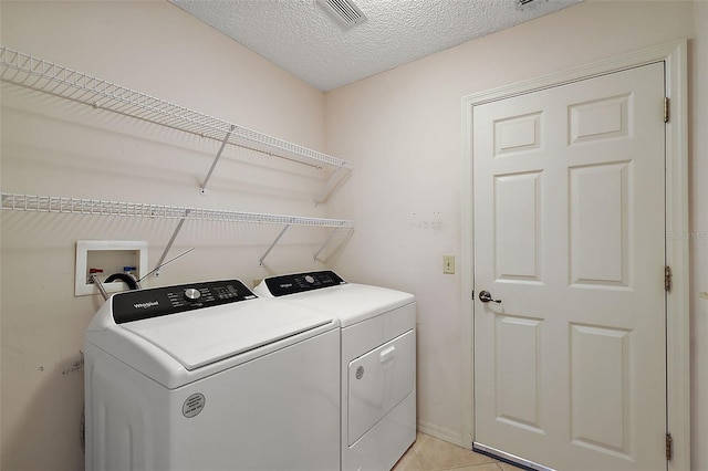 washroom with a textured ceiling, independent washer and dryer, and light tile patterned flooring