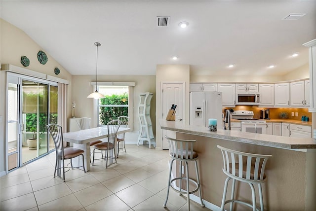 kitchen with white appliances, decorative light fixtures, white cabinetry, and a healthy amount of sunlight