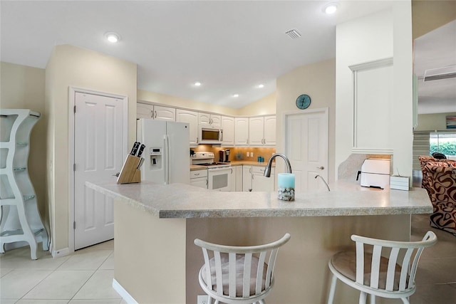 kitchen featuring kitchen peninsula, vaulted ceiling, white appliances, a breakfast bar area, and white cabinets