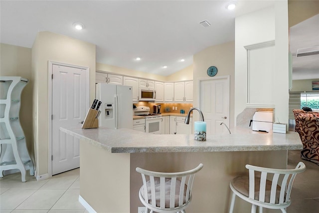 kitchen with white appliances, a breakfast bar, a peninsula, light countertops, and white cabinetry