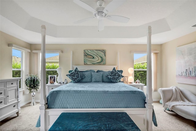 carpeted bedroom featuring a raised ceiling, multiple windows, and ceiling fan