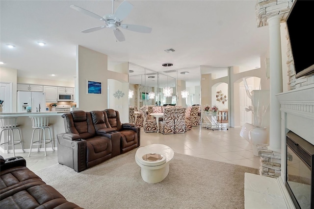 tiled living room featuring a stone fireplace and ceiling fan